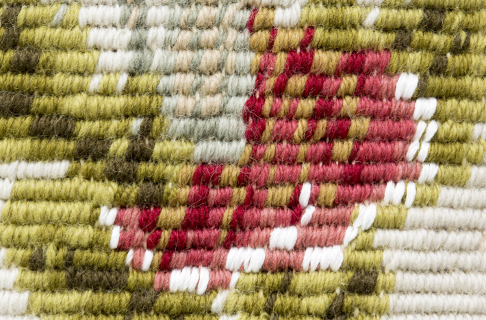 Fragement tkaniny zabytkowej. Jest to duże zbliżenie na czerwony kwiat i zielone liście. 